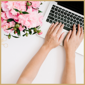 Image of a bunch of pink flowers beside a laptop and a woman's hands on the keyboard